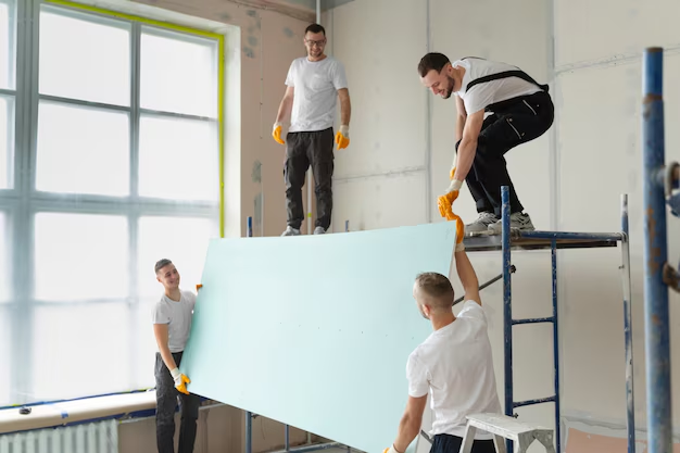 Team installing drywall inside a bright room with a big window